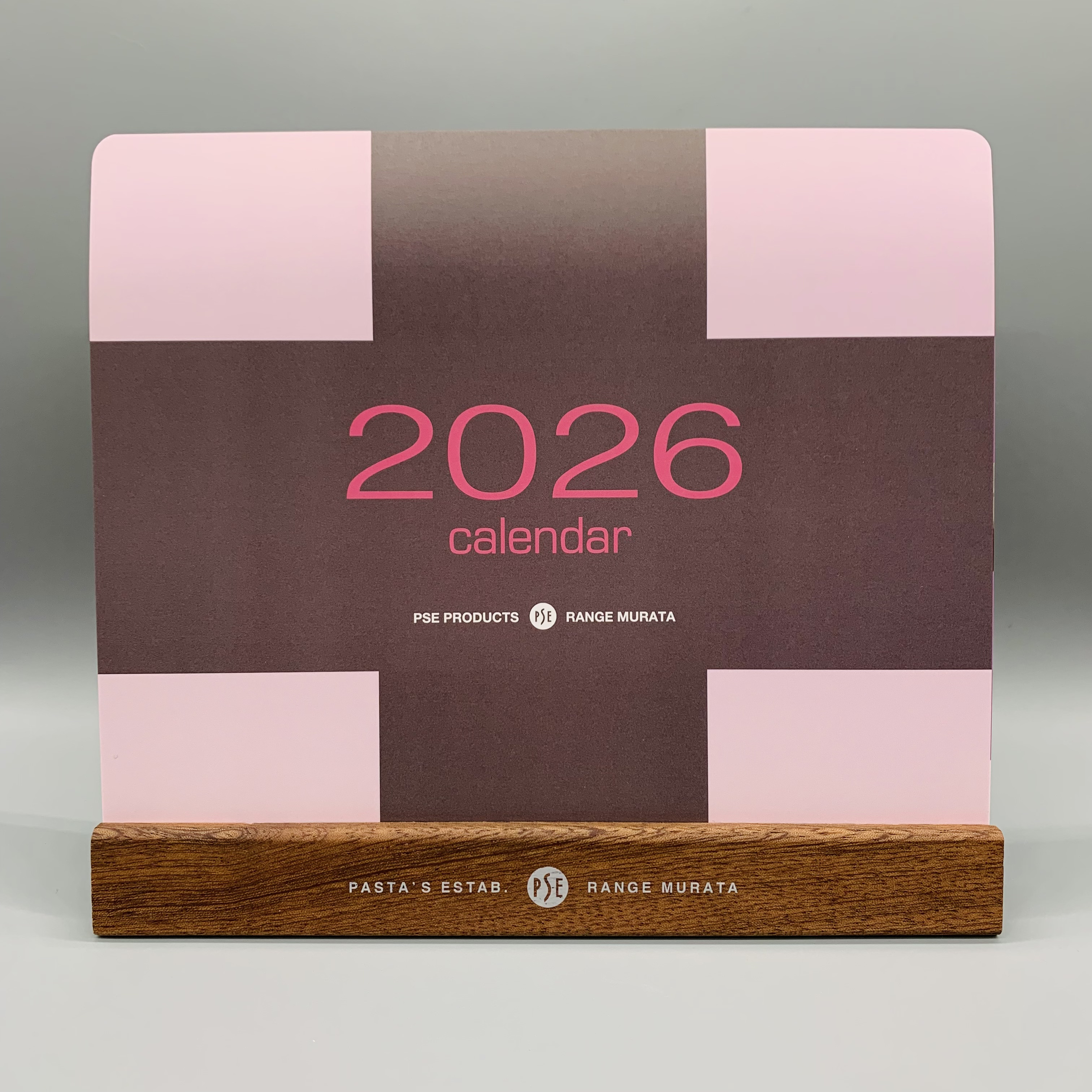 Desk calendar card printed with “2026 calendar” displayed upright in a wooden base.