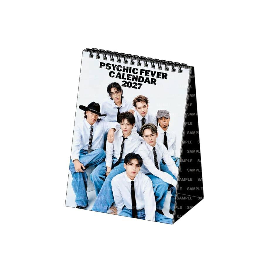 A PSYCHIC FEVER 2027 desk calendar standing upright showing a group photo of seven members on the cover.
