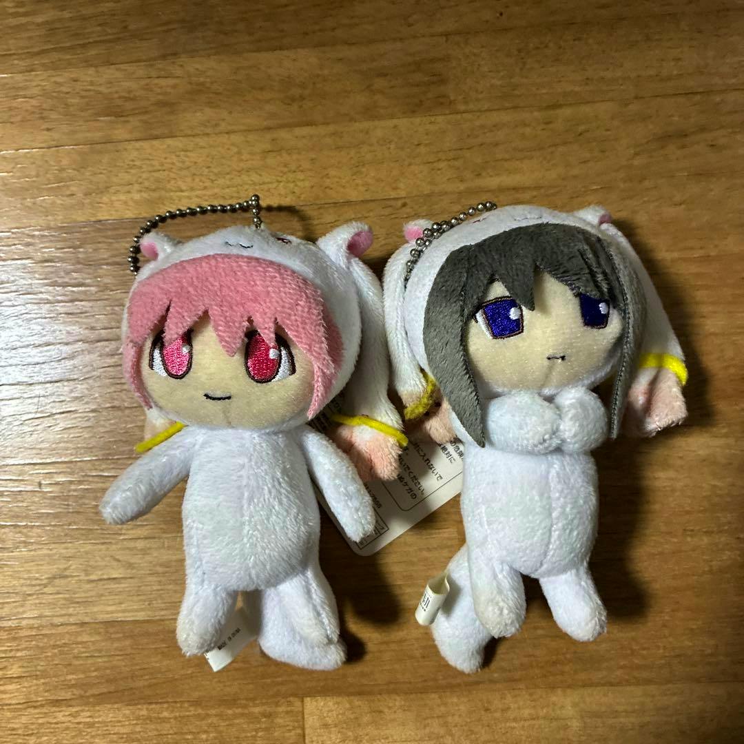 Two plush Kyubey kigurumi mascot keychains showing their front faces placed side by side on a wooden floor.