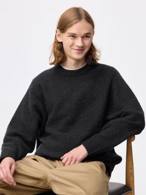 A seated model wearing a dark puff-knit pullover sweater.