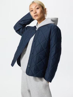 Model wearing a navy quilted no-collar women's jacket over a gray hoodie.