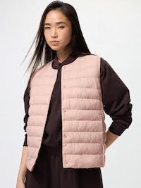 Model wearing a light pink quilted nylon vest over a dark long-sleeve top.