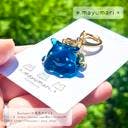 A blue glitter octopus-shaped keychain with gold hardware displayed on a white branded card held in a hand.