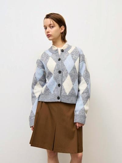 Model wearing a grey, blue, and white argyle crew-neck cardigan buttoned over a brown skirt.
