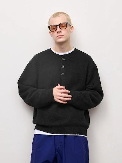A model wearing a black henley-neck knit sweater with three buttons visible.