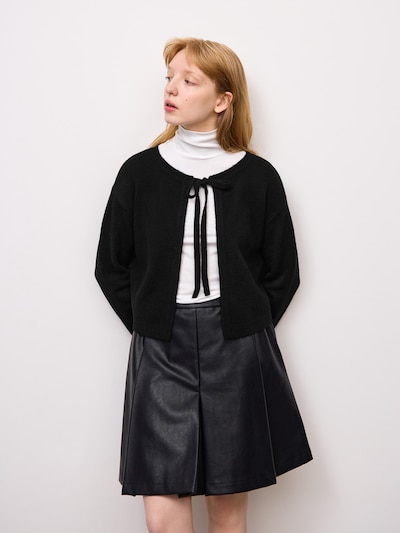 Model wearing a black knit ribbon cardigan over a white turtleneck and a black skirt.