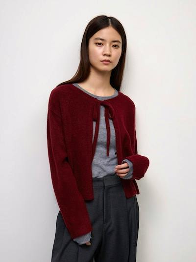 Model wearing the puffy-touch knit ribbon cardigan in burgundy tied at the neck over a gray top.