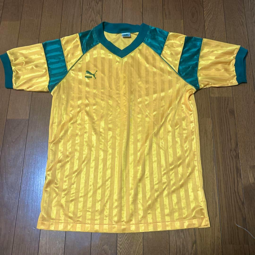 Yellow and green PUMA game shirt laid flat on a wooden floor, showing front and sleeves.