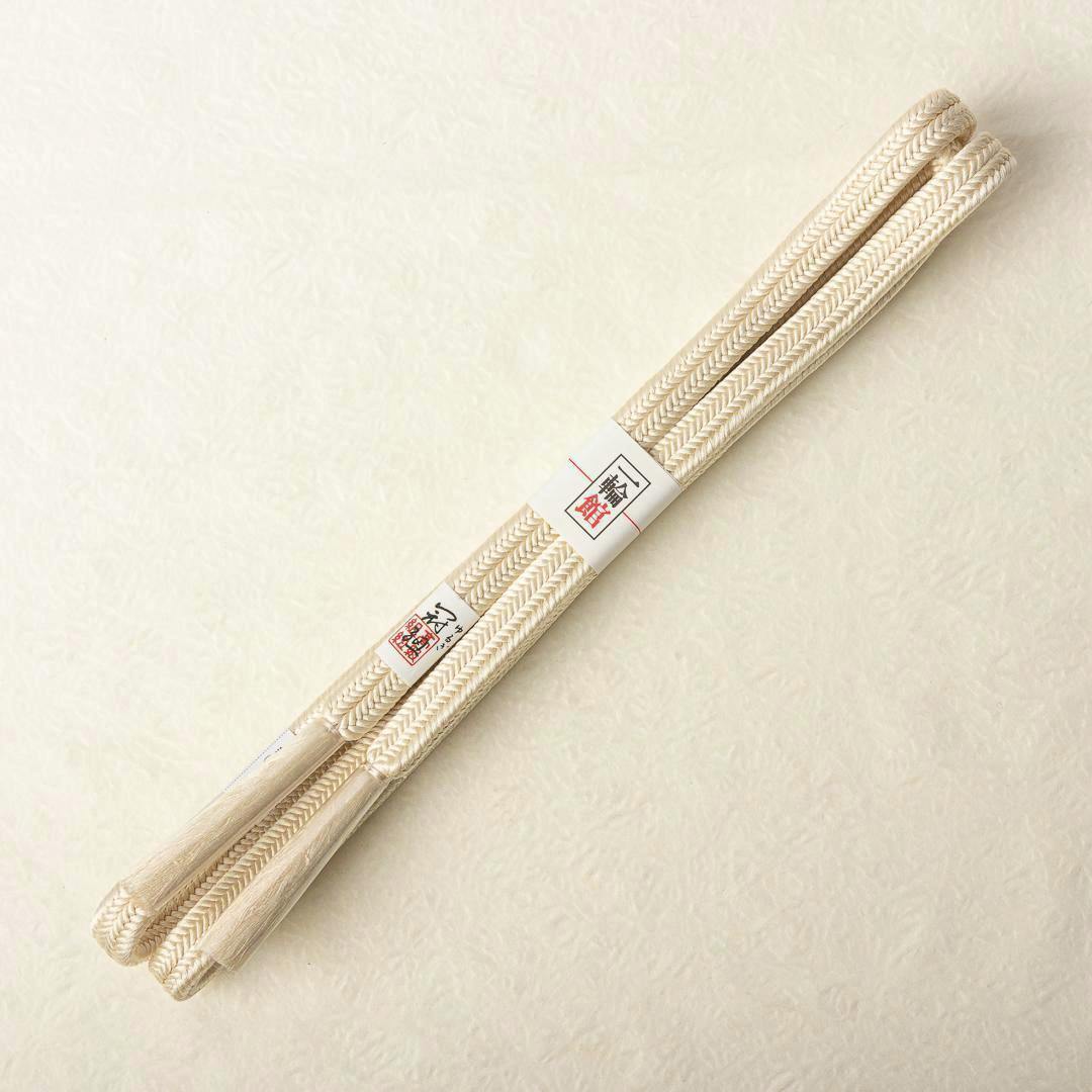 Ivory silk braided obijime (帯締め) with a small paper label laid on a light textured background.