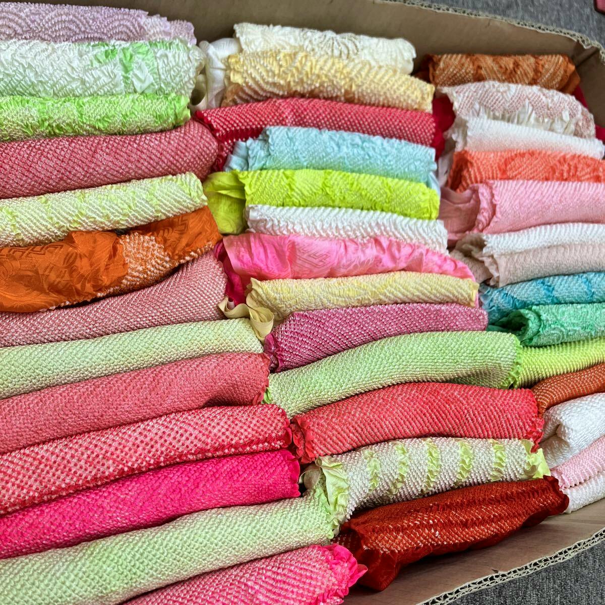 Multiple folded colorful obiage (帯揚げ) pieces arranged in a box, showing various shibori textures and colors.