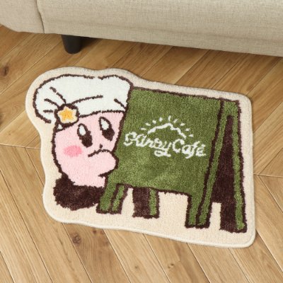 A Kirby-themed embroidered room floor mat with a green sign reading "Kirby Café" placed on a wooden floor next to a sofa.