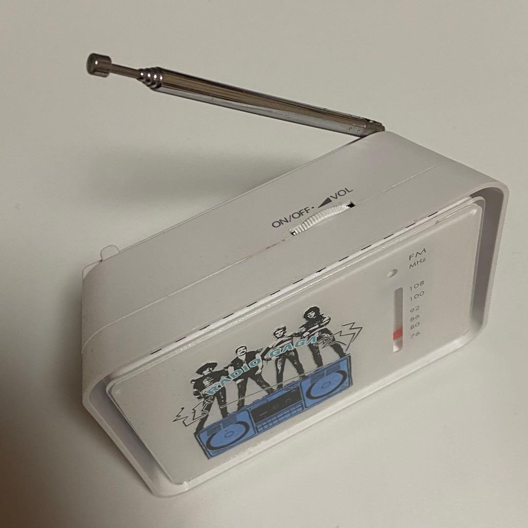 White Queen Radio Gaga radio shown at an angle with its antenna extended and the front illustration of band figures and a blue boombox visible.