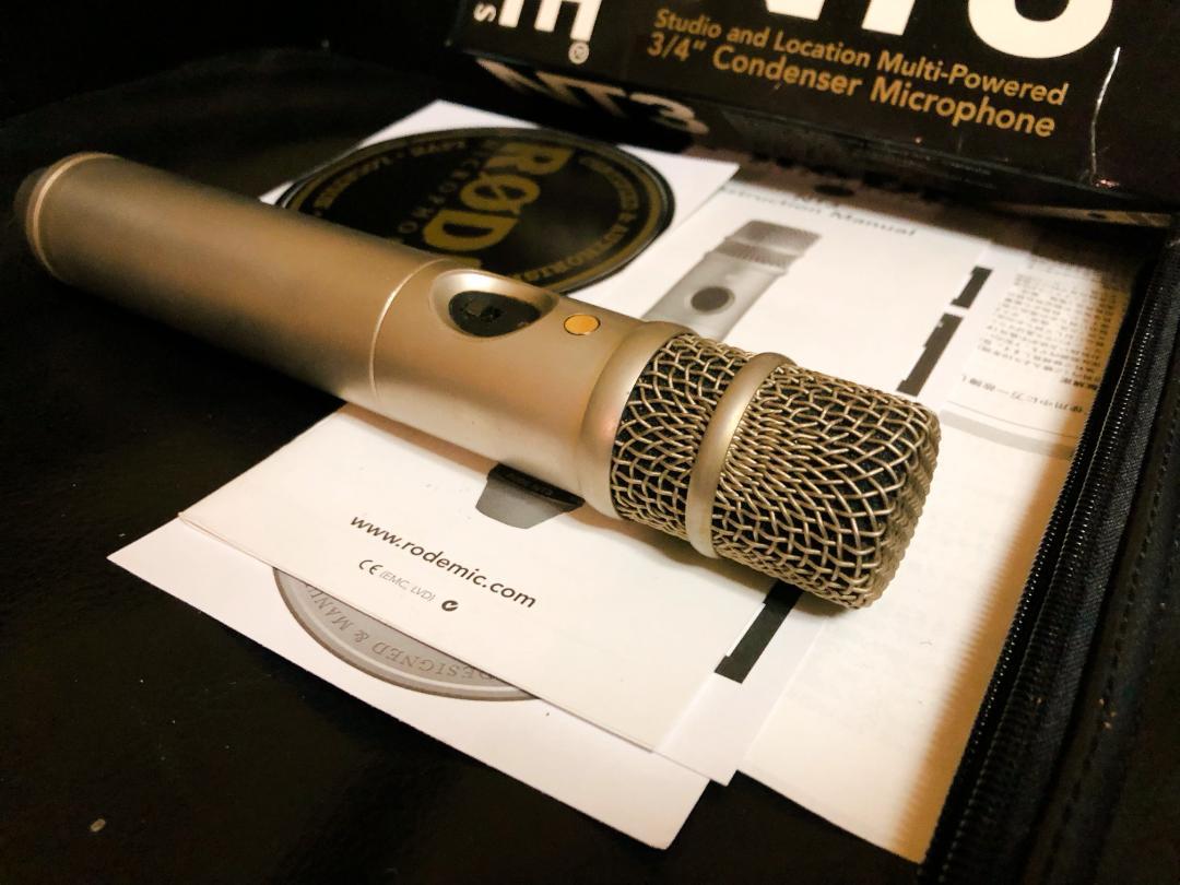 A Rode NT3 condenser microphone lying on paperwork with its original box partially visible behind it.