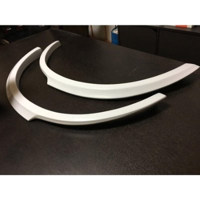 Two white R34 4-door rear fender arches placed on a dark table.