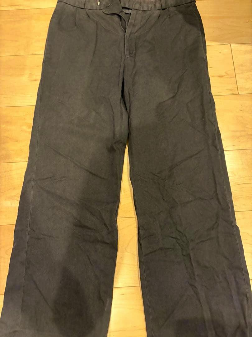 Black wide-leg cotton men's slacks laid flat on a wooden floor, front view.