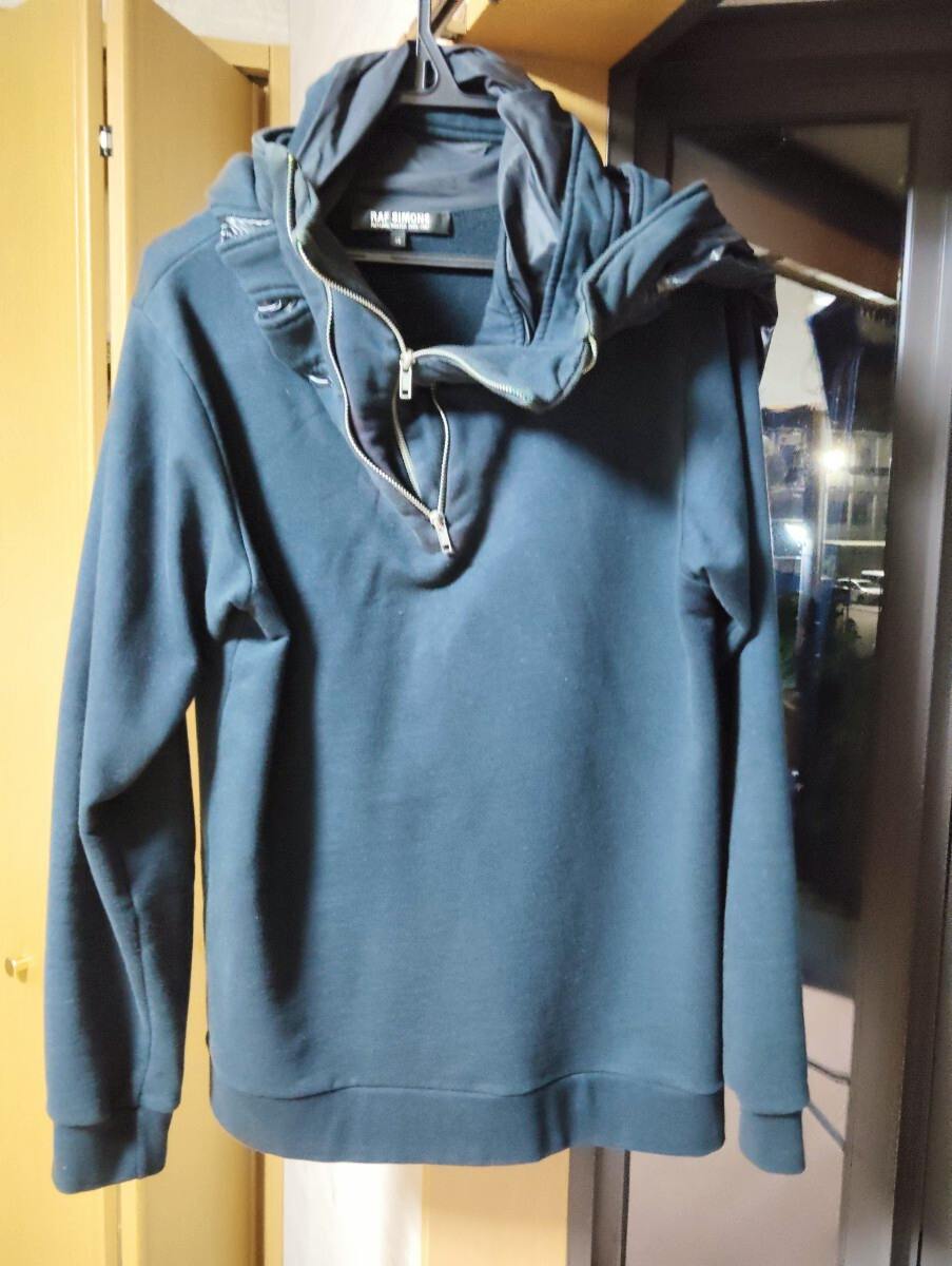 Dark Raf Simons cotton zip hoodie hanging on a hanger, front view visible.