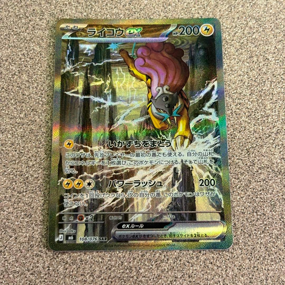 Photograph of the ライコウex trading card (108/076 SAR) showing the card front holofoil while lying on a textured surface.