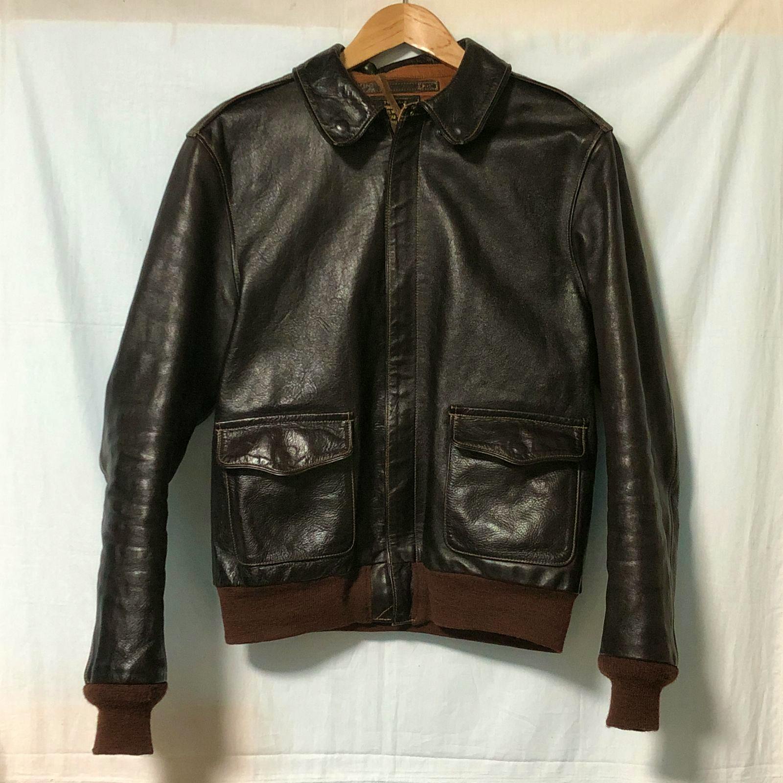 Front view of a dark brown cow leather Type A-2 flight jacket hanging on a wooden hanger.
