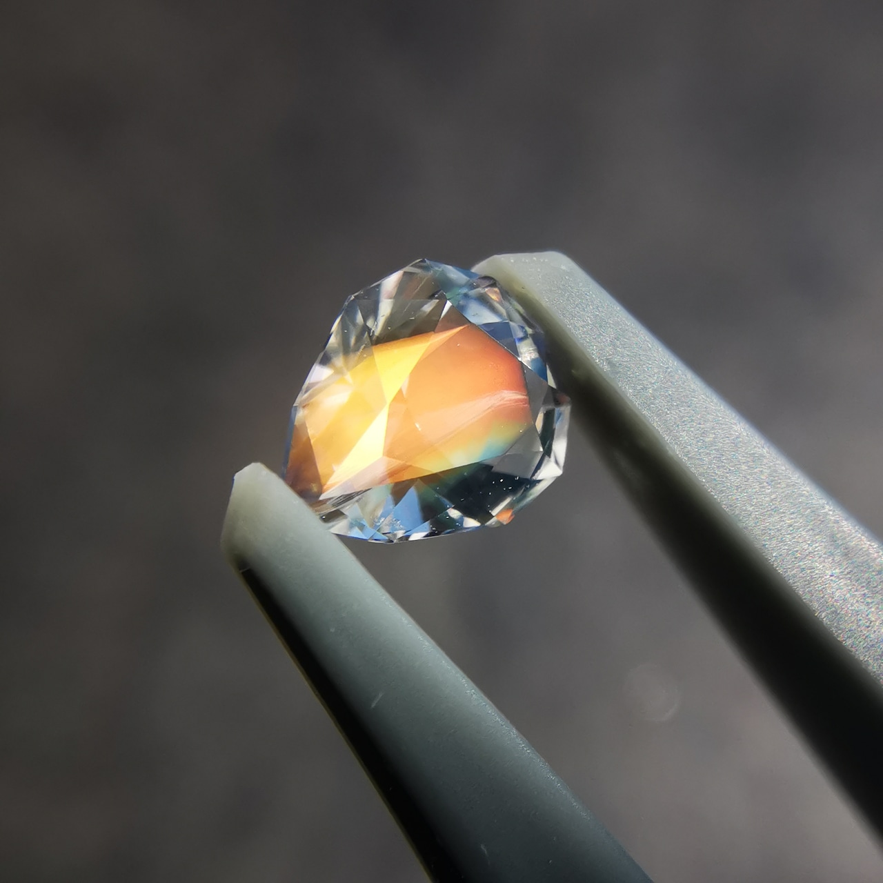 Close-up of a faceted rainbow moonstone gemstone held in tweezers showing colorful iridescence.