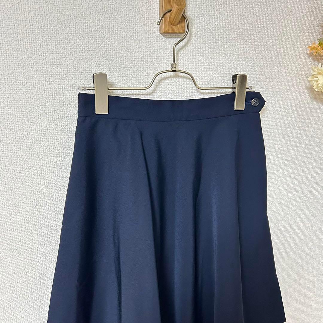 Navy flared knee-length women's wool skirt hanging on a hanger against a light textured wall.