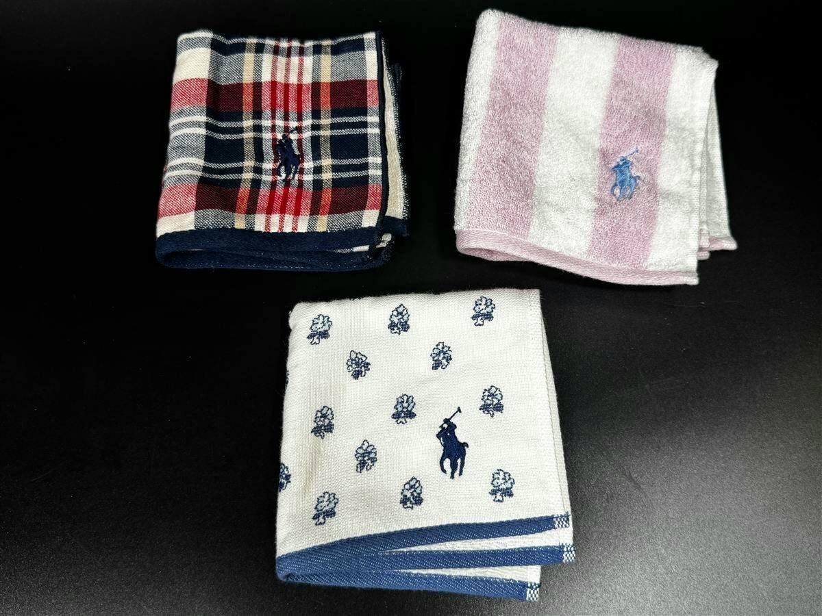 Three folded Ralph Lauren cotton hand towels with pony embroidery — a red/navy plaid, a pink-and-white striped, and a white towel with blue motifs — on a black background.
