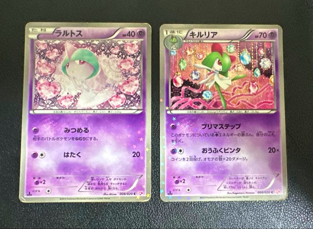 Fronts of two Pokémon trading cards (Ralts and Kirlia) placed side by side on a dark surface.