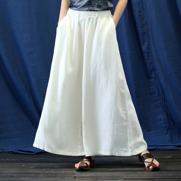 A front view of a model wearing white wide women's cotton pants with an elastic waistband and pockets against a dark blue backdrop.