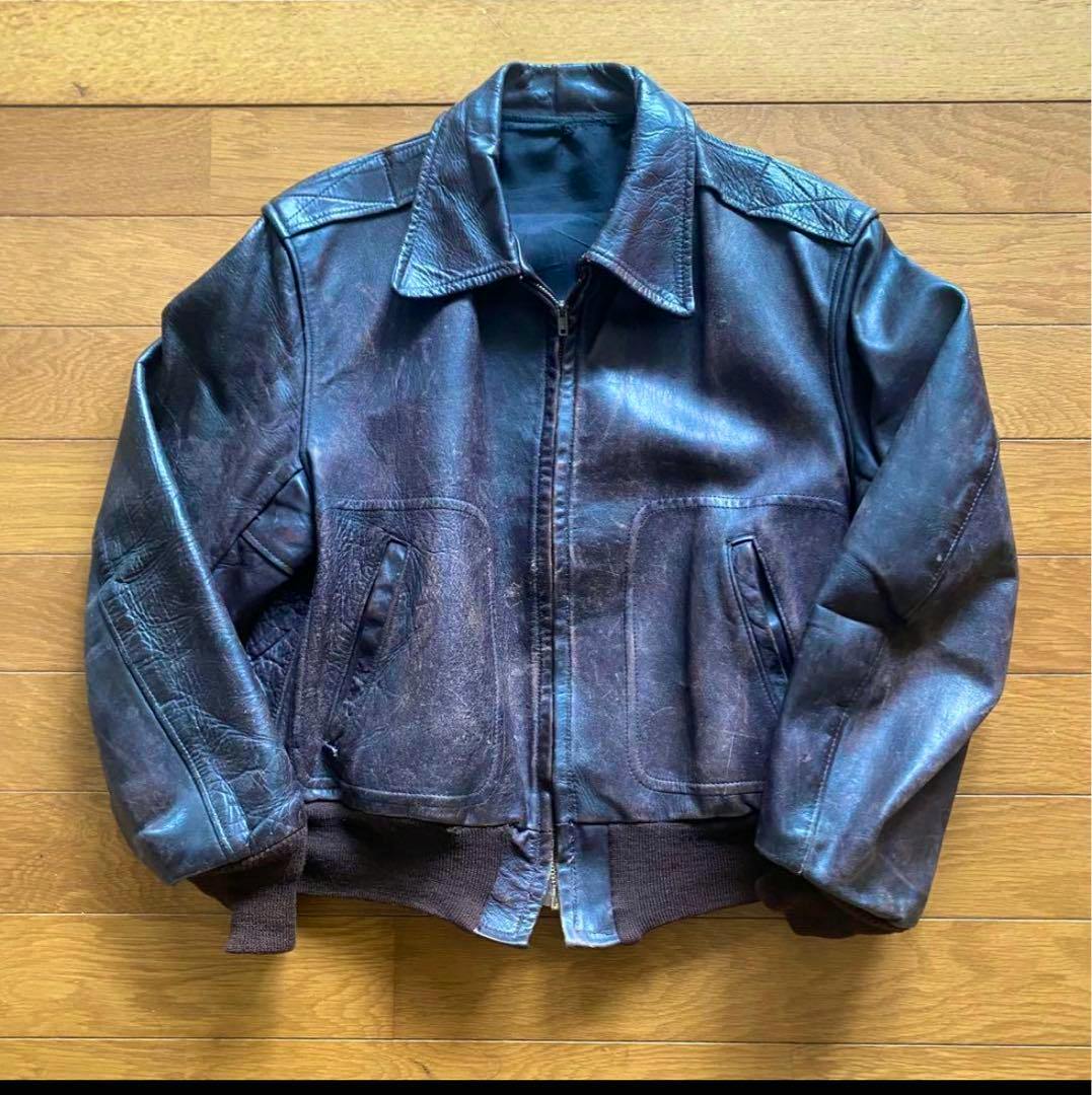 Front view of a vintage short-length men's A-2–style cow leather jacket laid flat on a wooden floor.