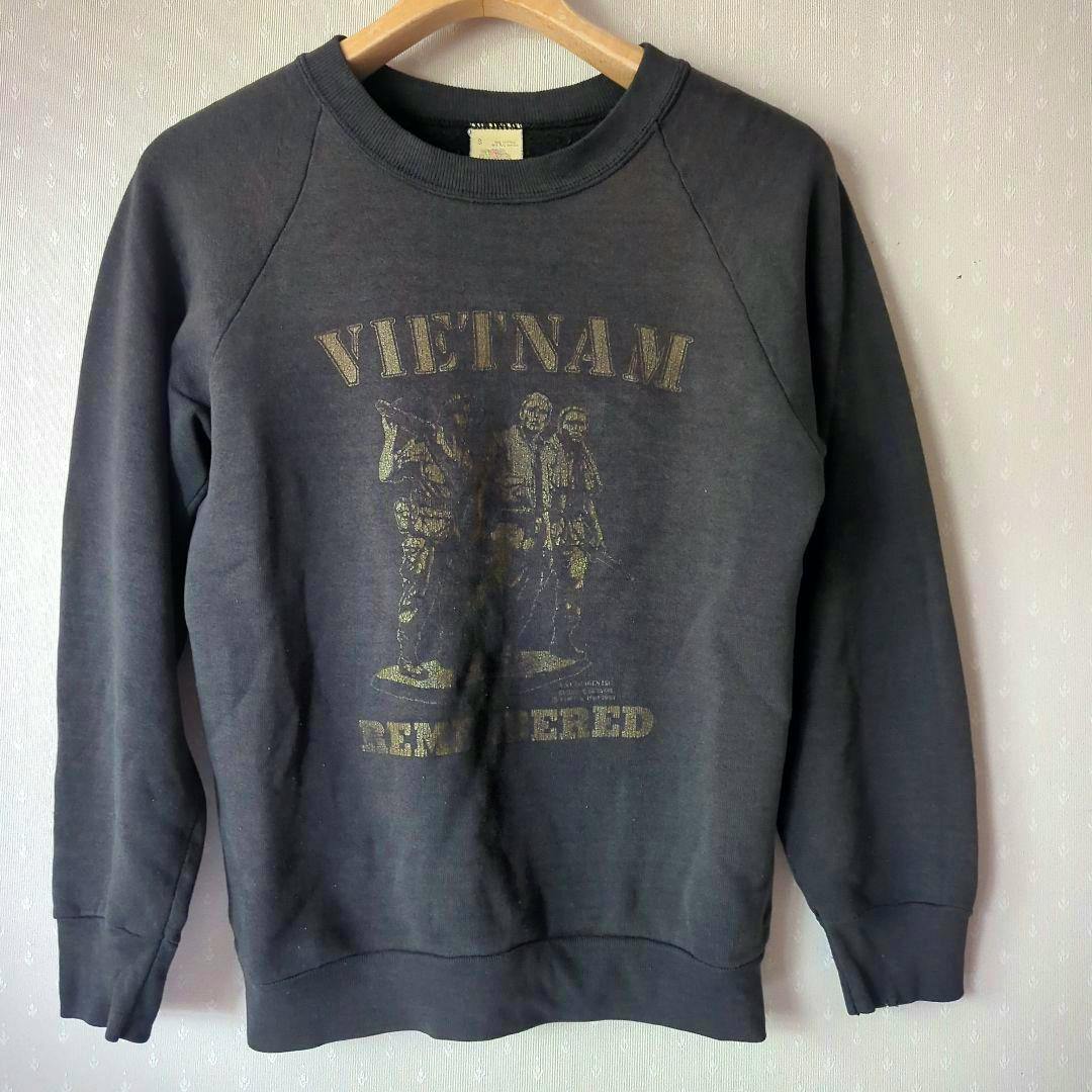 Front view of a faded dark cotton men’s pullover sweatshirt with a 'VIETNAM' graphic and two soldiers printed on the chest, hanging on a hanger.