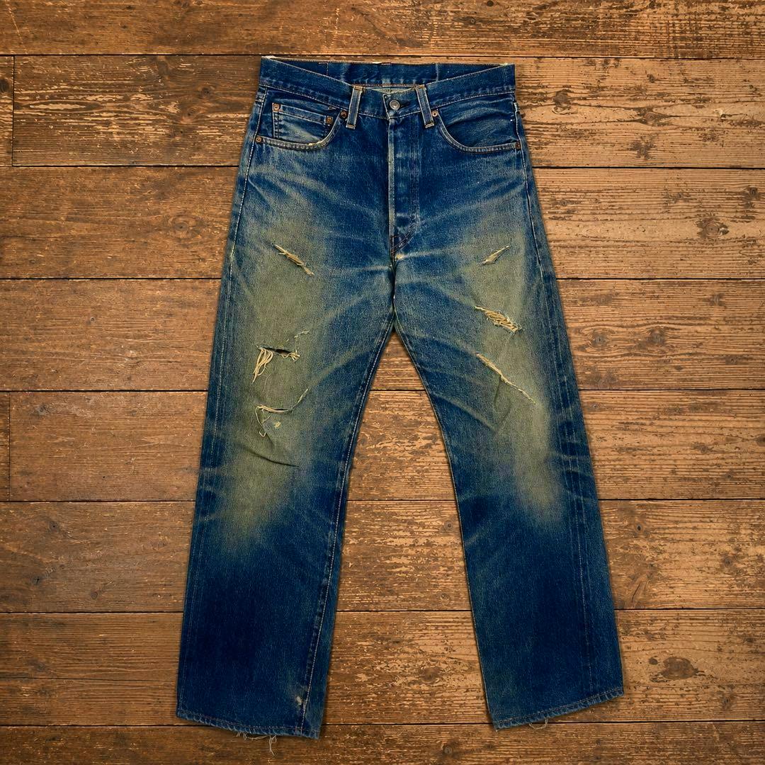 Front view of the men's denim jeans laid flat on a wooden floor showing fading and ripped knees.