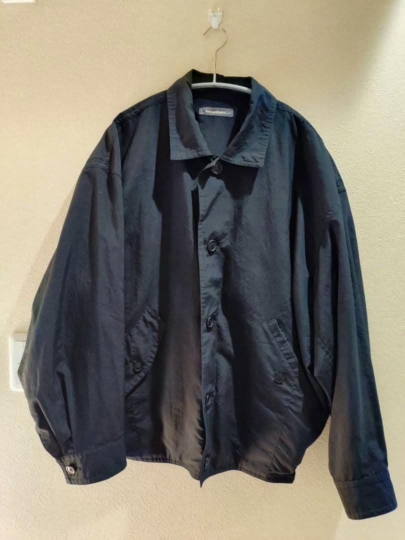 Front view of a black Issey Miyake men's polyester jacket hanging on a hanger against a wall.