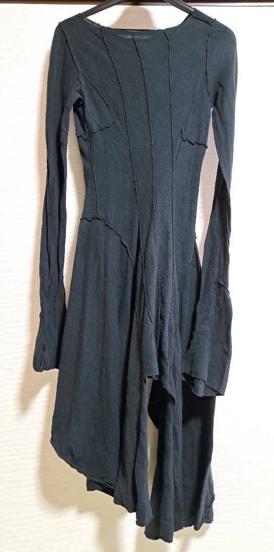 Black knit women's cotton dress (Alice Auaa) with long sleeves and an asymmetric hem hanging on a hanger against a light wall.