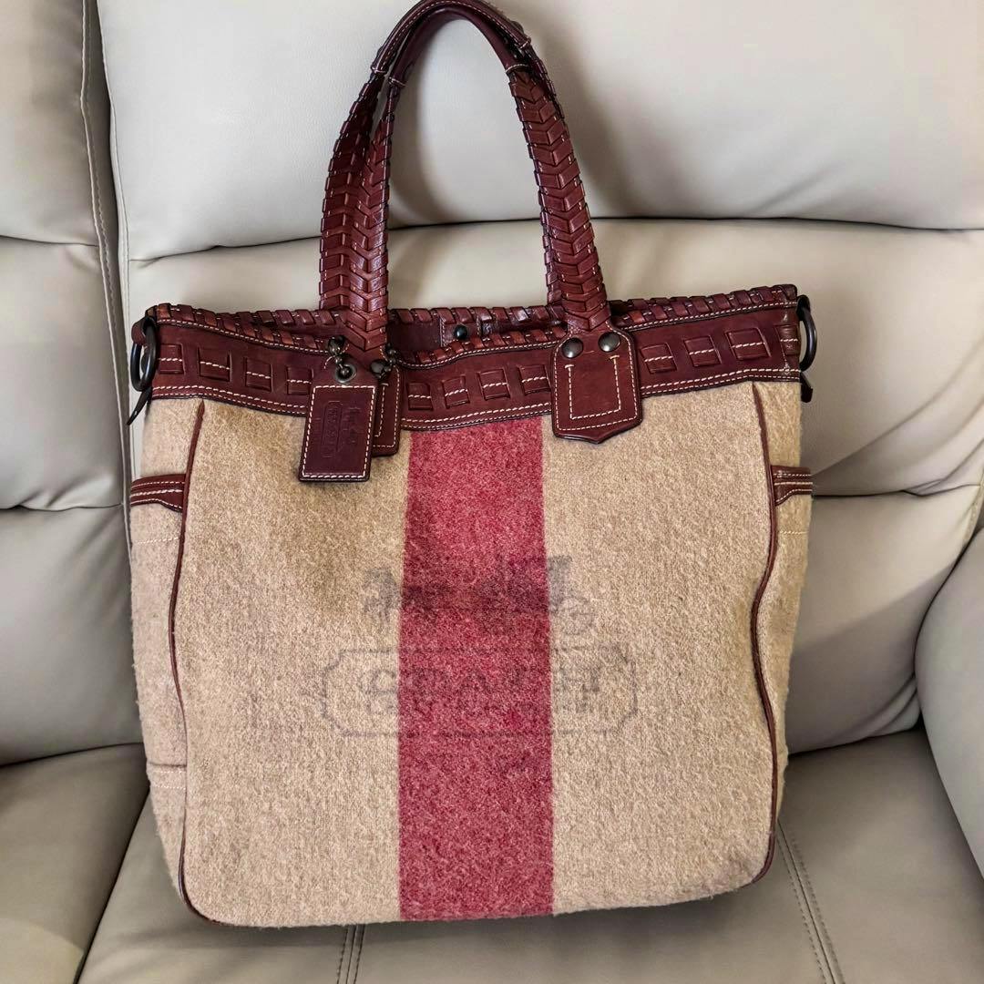 Front view of a Coach canvas tote bag with brown leather trim and a central red stripe.