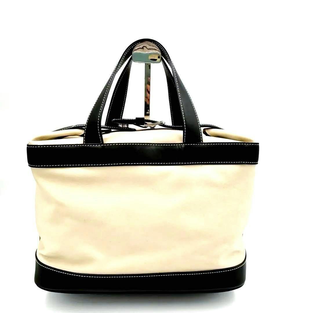 Front view of a COACH cream canvas handbag with black leather trim and handles.