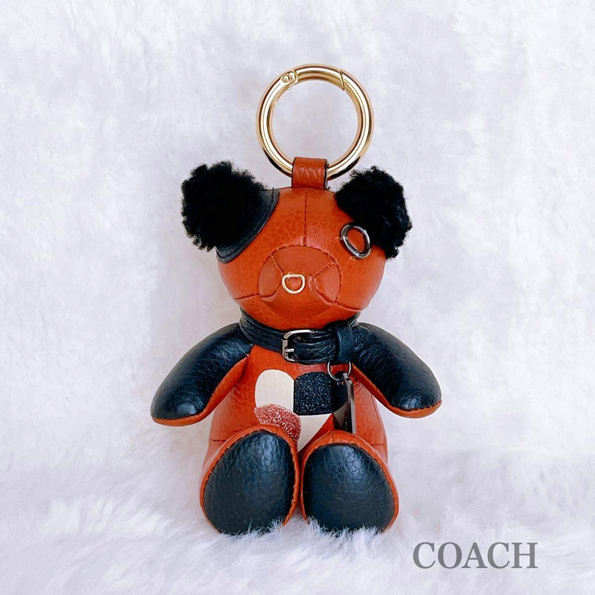 Front view of a Coach leather bear bag charm keyring with black accents, a patchwork heart on the body, and a gold-tone key ring.