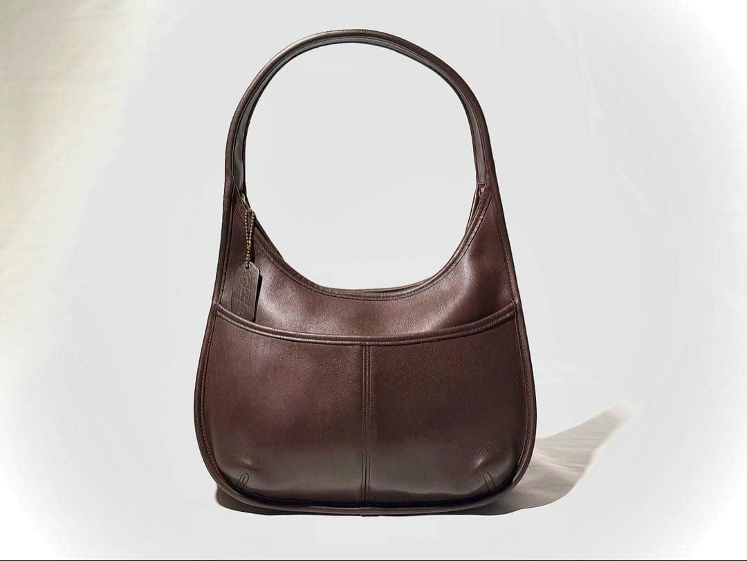 Front view of a brown COACH one-shoulder leather bag placed on a white background.