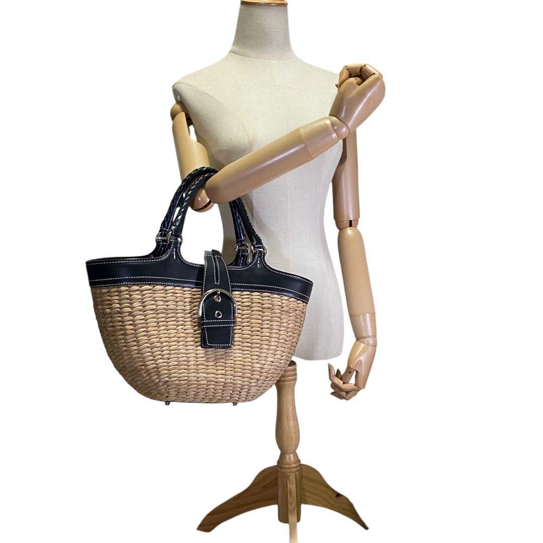 Woven basket handbag with black leather trim and front buckle hanging from a mannequin arm