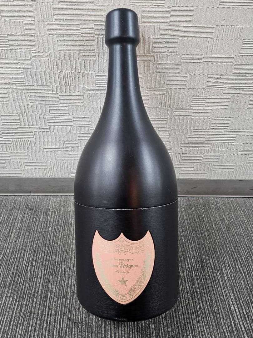 Front view of a black bottle-shaped plastic container with a pink Dom Pérignon rosé 1998 shield label on the front.