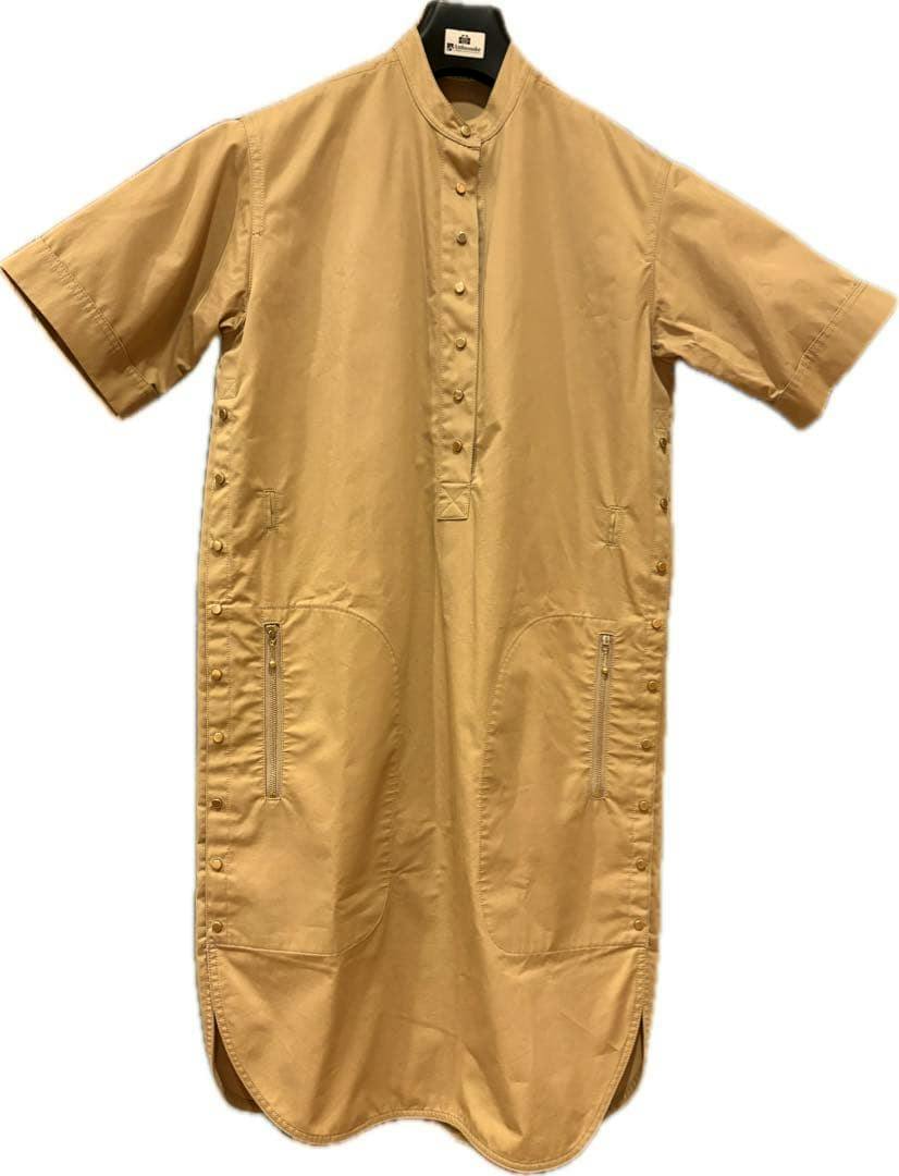 Front view of a tan cotton women's dress on a hanger, showing short sleeves, a central button placket, and two zippered front pockets.