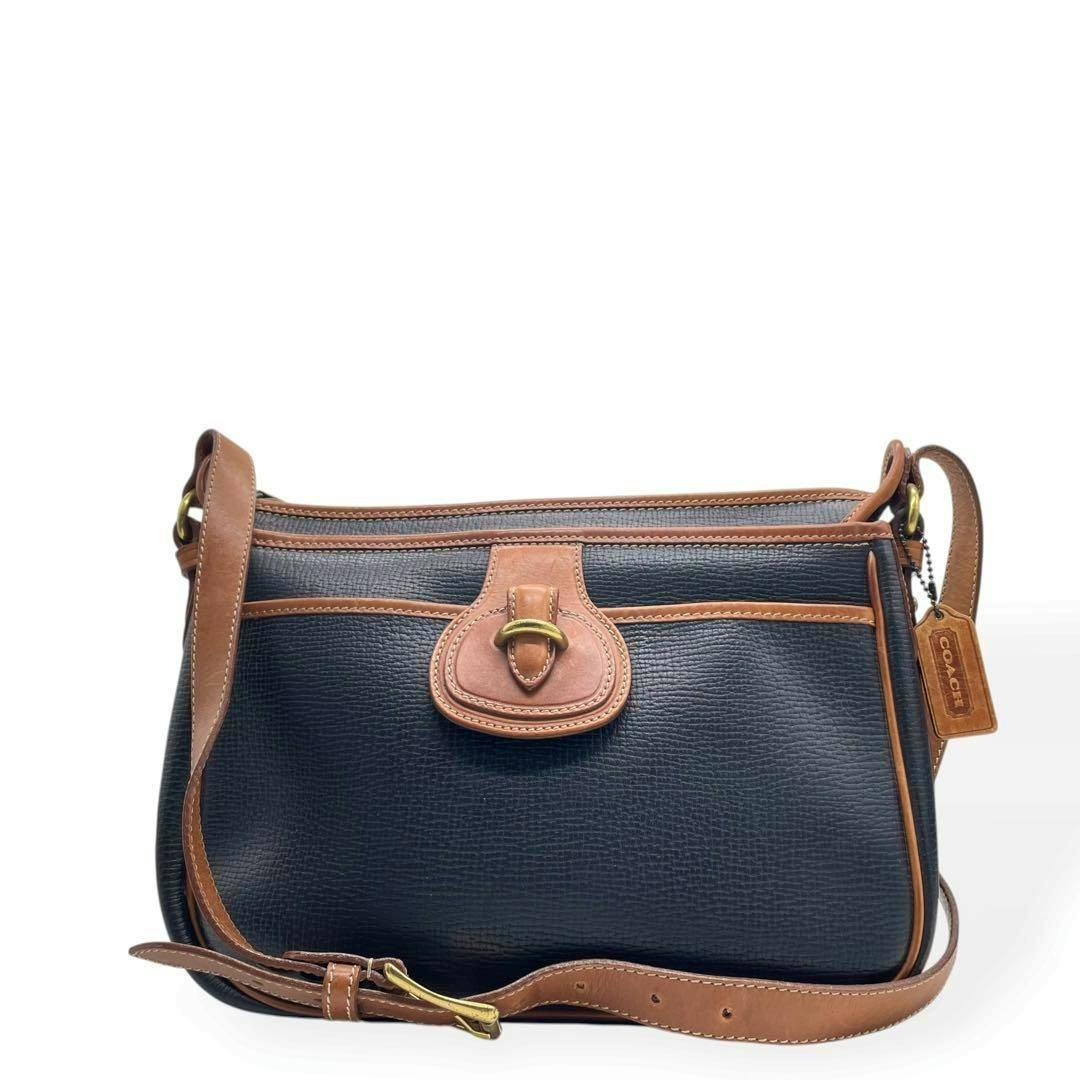 Front view of a Coach Sheridan leather shoulder handbag with a dark navy body, brown leather trim, adjustable strap, and Coach tag.