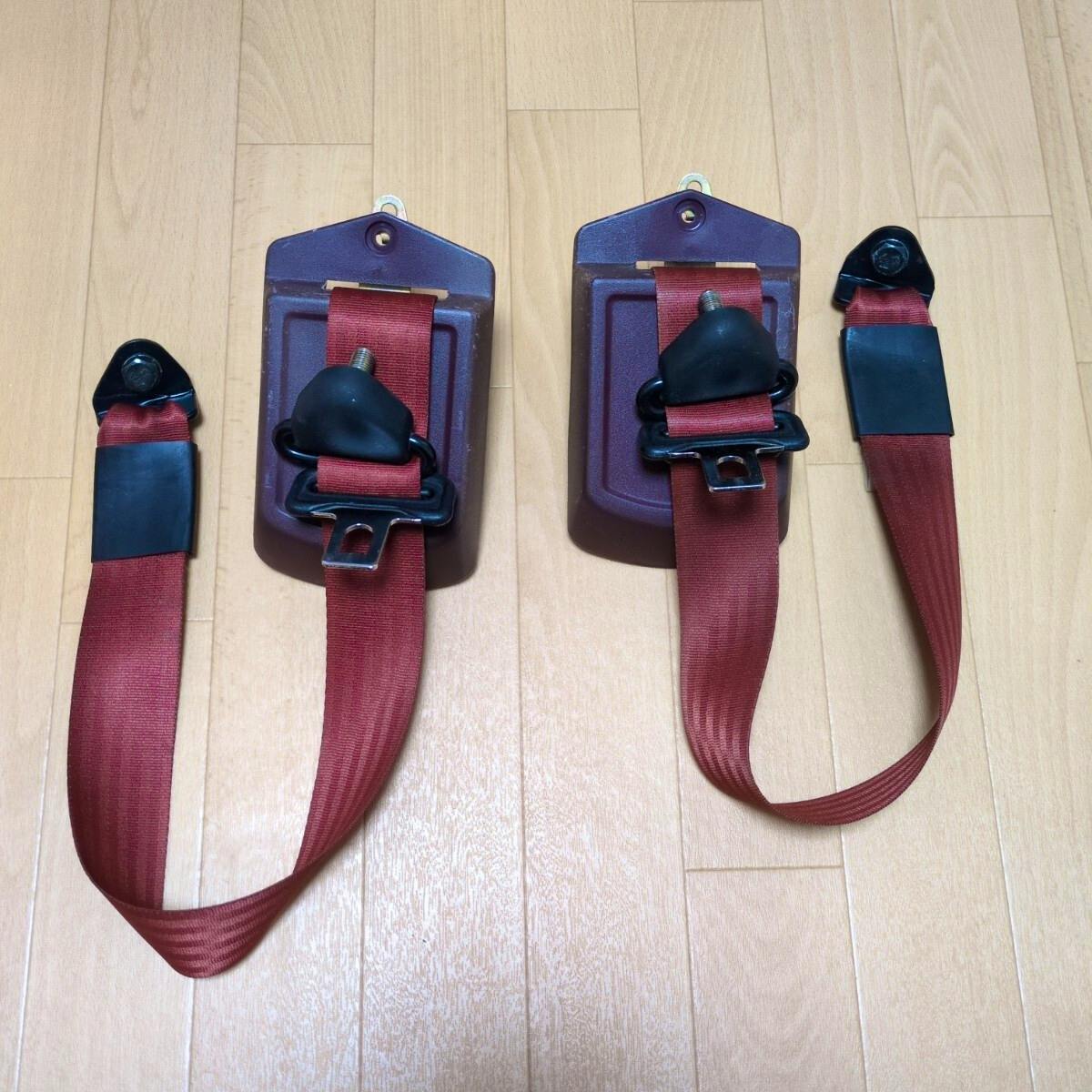 Two red front seat belt assemblies for a Honda Acty laid on a wooden floor.
