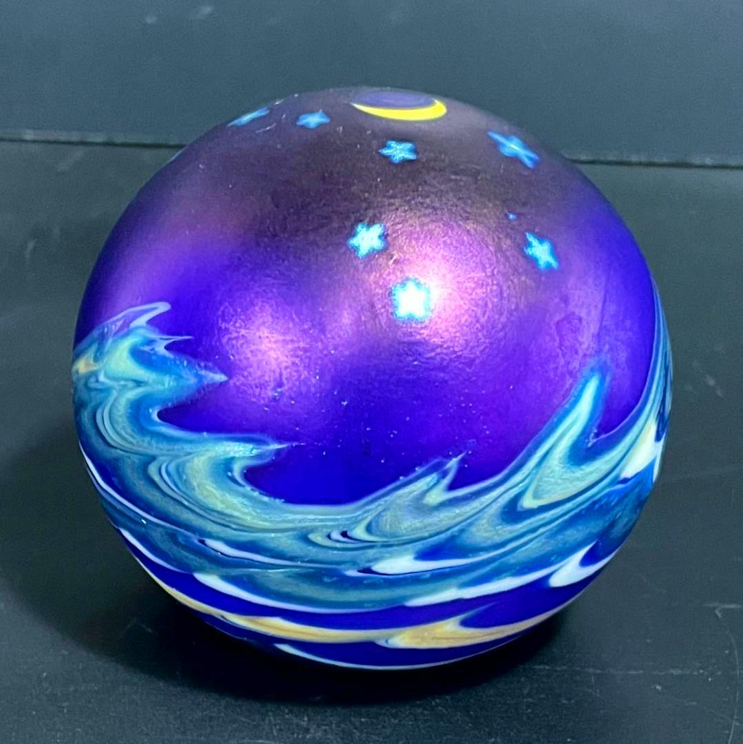 Glass paperweight showing a purple night sky with a crescent moon, stars, and swirling blue wave patterns.