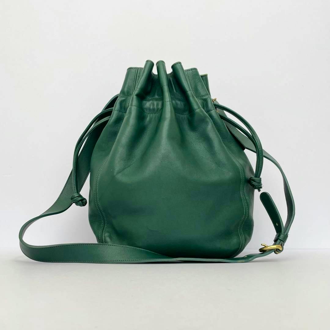 Green cow-leather drawstring shoulder bag on a white background, front view showing the strap and brass buckle.
