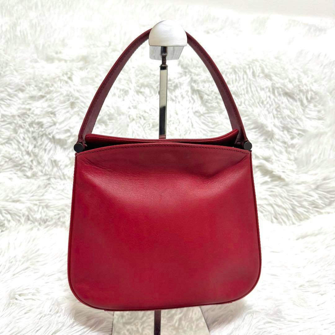 Front view of the vintage red Coach cow leather handbag with a short top handle displayed on a stand.