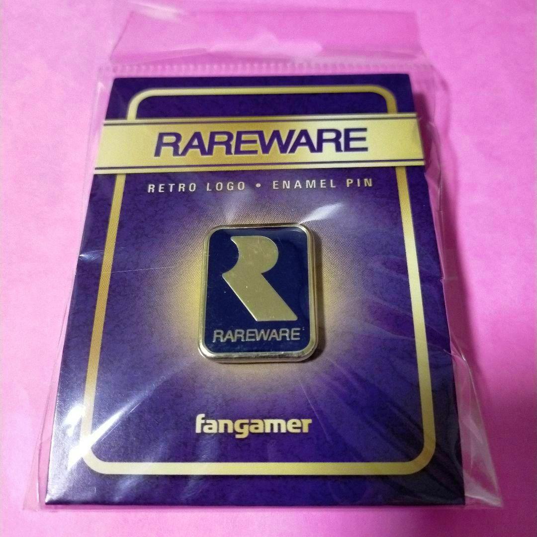 A Rareware enamel pin on its purple backing card inside clear plastic packaging, shown against a pink background.