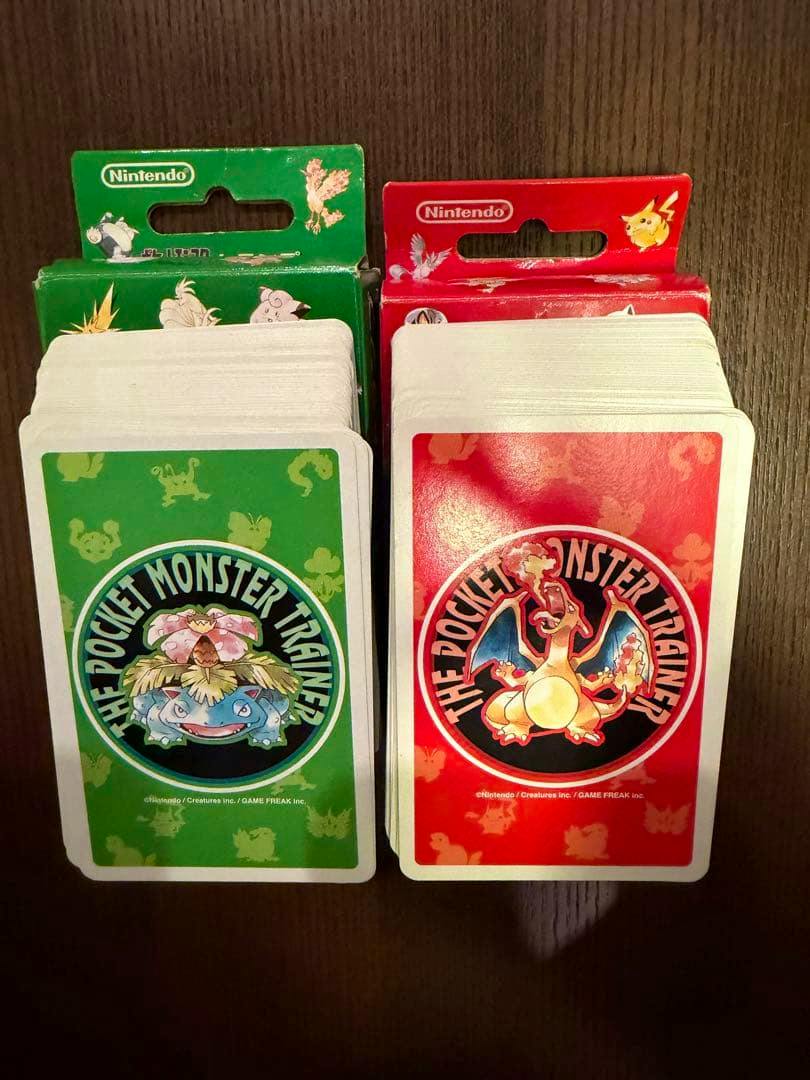 Two stacks of Pokémon trump cards showing green Venusaur and red Charizard backs with their packaging behind.
