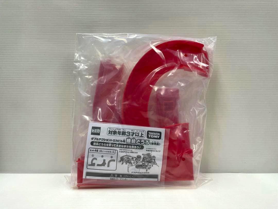 Red plastic connector road pieces for a Tomica building set pictured in a clear sealed bag with a printed instruction insert.