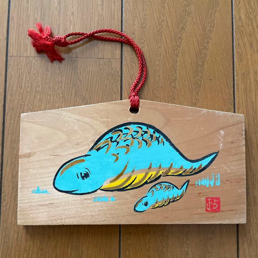 Front of a wooden ema plaque painted with two blue tsuchinoko figures and a red hanging cord.