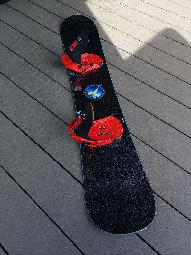 Burton snowboard with red bindings mounted on a black top sheet showing a circular space graphic.