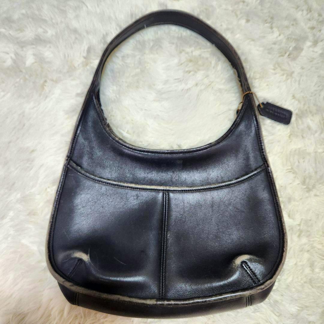 Front view of a black cow leather Coach shoulder bag with a single curved handle on a light fur background.